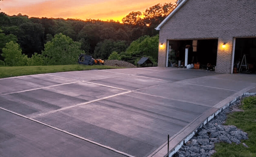 Concrete driveway installation with sunset background and adjacent home, showcasing completed concrete work by JL Home Builders.