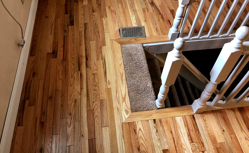Natural hardwood flooring installation with a transition to carpeted staircase, showcasing quality craftsmanship in home remodeling.
