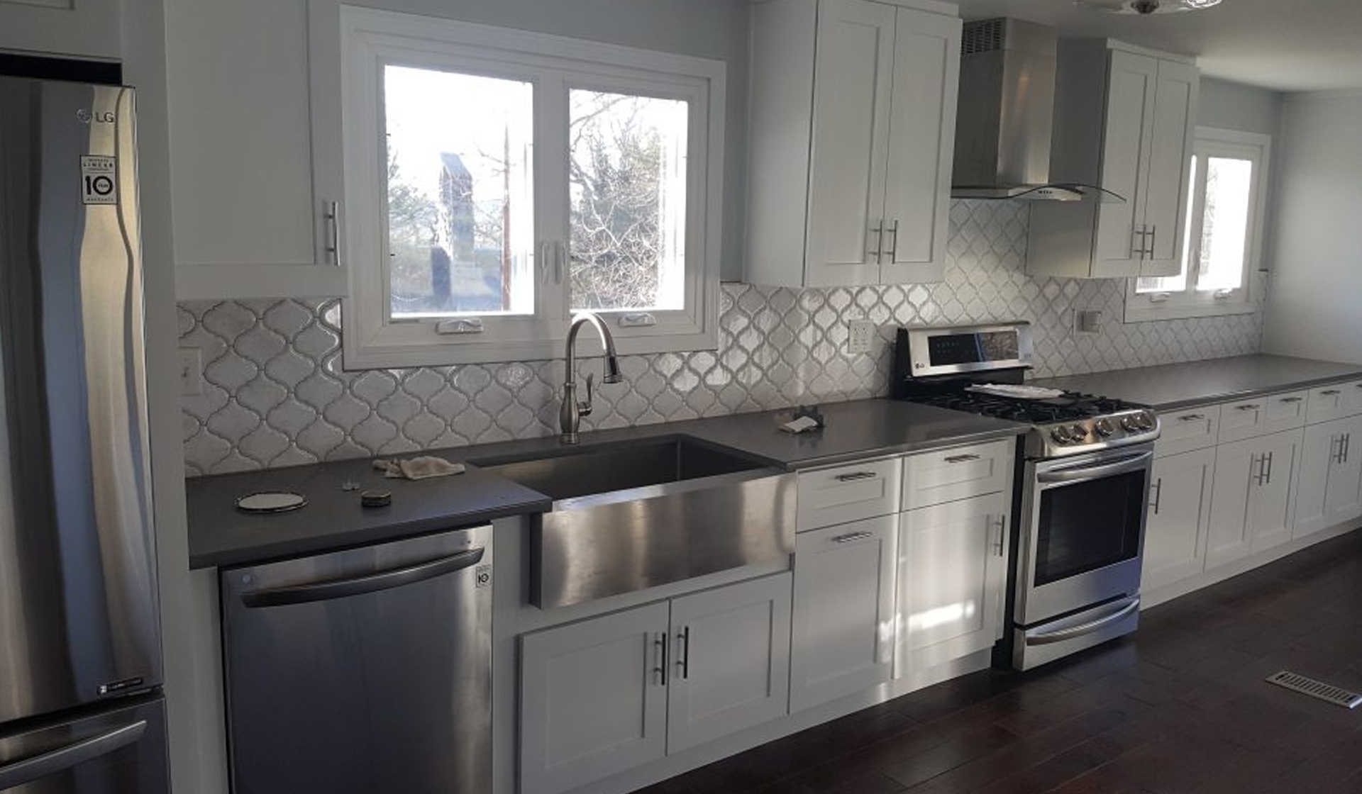 Modern kitchen featuring stainless steel appliances, white cabinetry, gray countertops, and decorative tile backsplash, illustrating JL Home Builders' kitchen remodeling services.