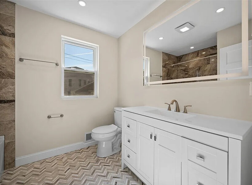 Modern bathroom featuring a white vanity with double sinks, a large mirror, and natural light from a window, showcasing elegant tile work and a clean, spacious design ideal for bathroom remodeling.
