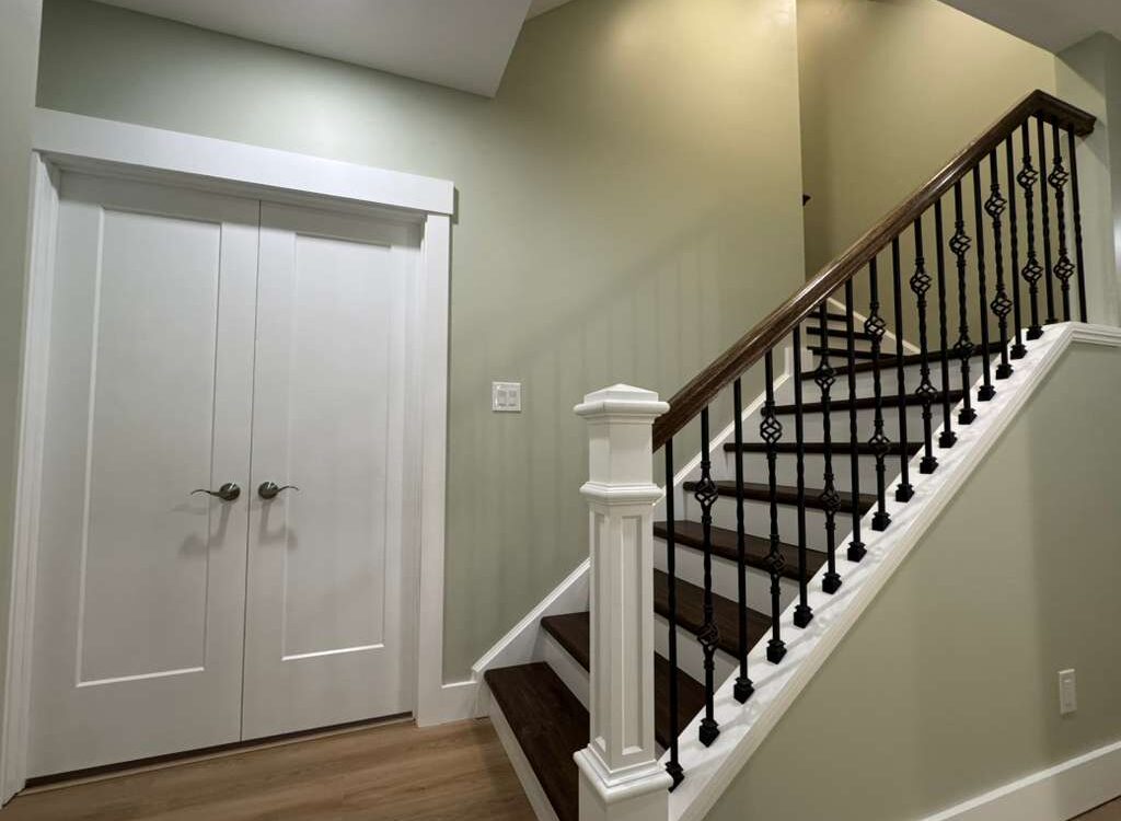Staircase with elegant black iron railing and white trim, leading to an upper level, adjacent to double doors in a renovated Pittsburgh home interior.