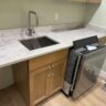 Kitchen countertop with stainless steel sink, wooden cabinetry, and a dishwasher, illustrating potential upgrades for energy-efficient home improvements in Pittsburgh.