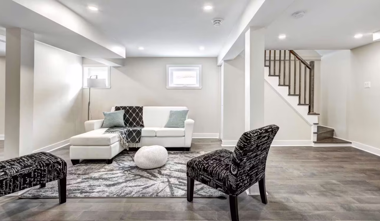 Finished basement living area with modern flooring, recessed lighting, seating, and an open staircase.