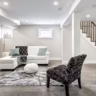 Finished basement living area with modern flooring, recessed lighting, seating, and an open staircase.