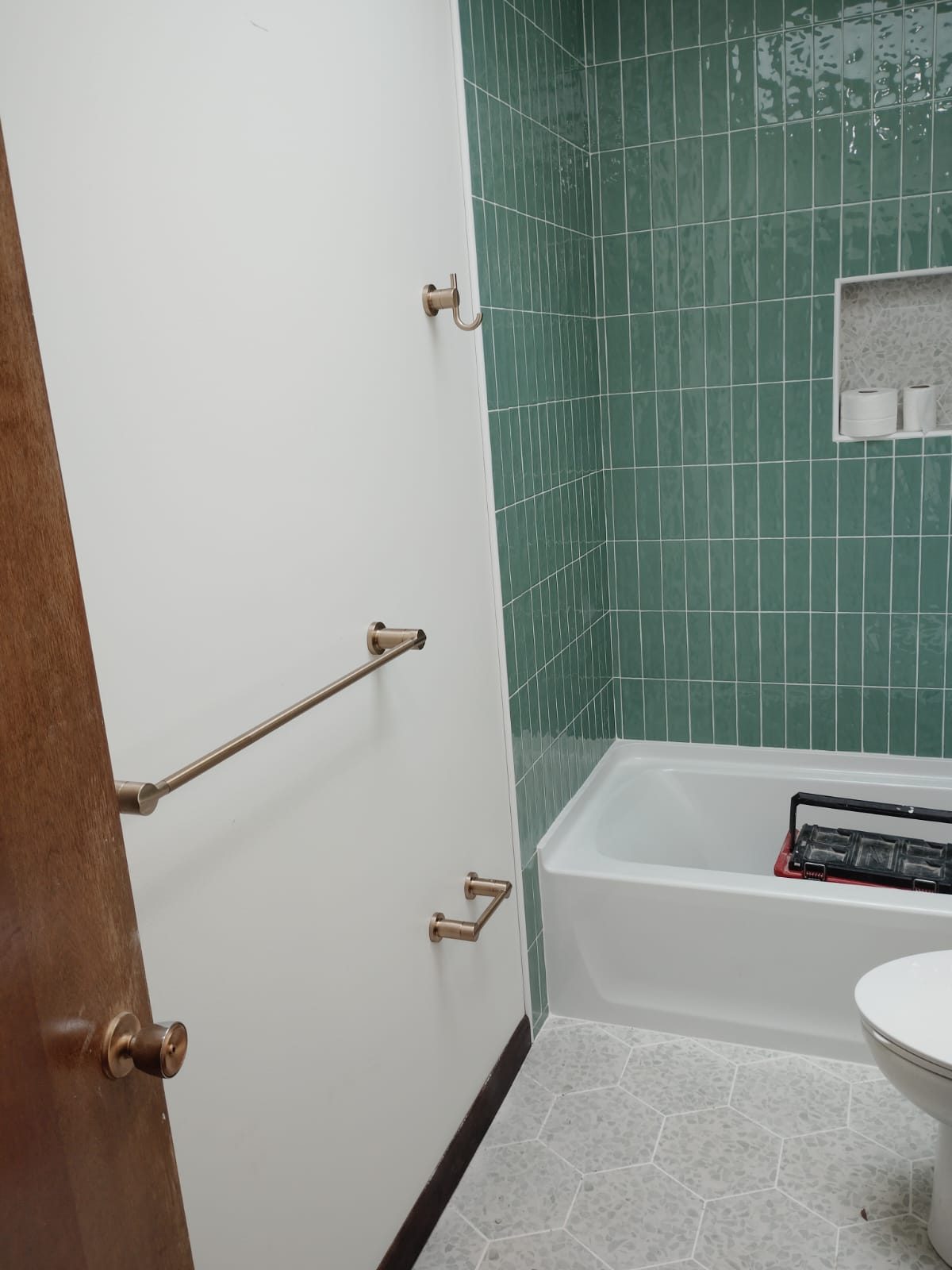 Bathroom with green vertical tile around a white tub, a tiled niche and brass towel bars