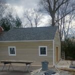 Building with new lap siding, two windows and a gray shingle roof, with sawhorses outside