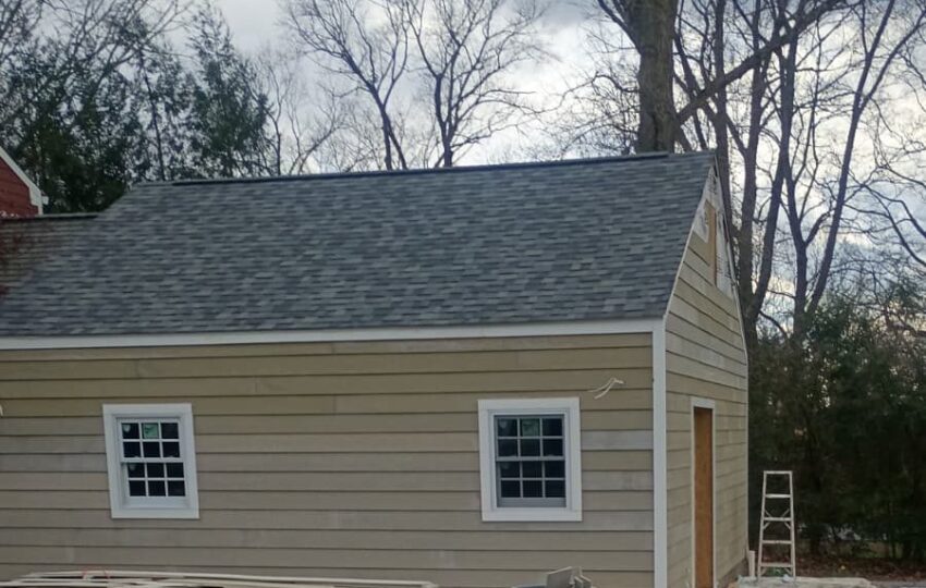 Building with new lap siding, two windows and a gray shingle roof, with sawhorses outside