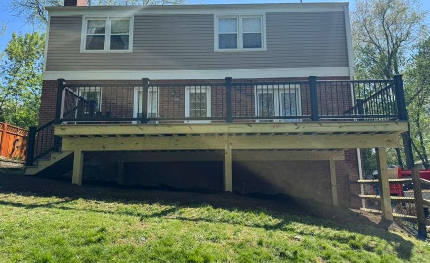 Rear view of a raised deck with gray decking and black railings on a brick home