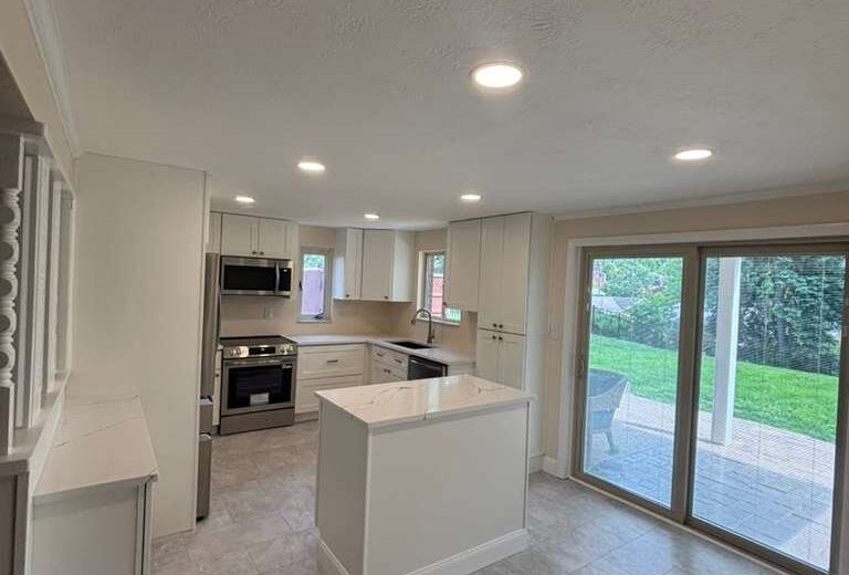 White kitchen with a center island, stainless appliances and sliding glass doors