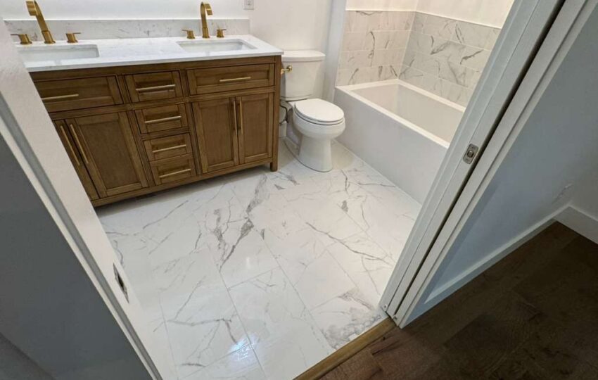 Remodeled bathroom with a wood double vanity, gold faucets, white tub and marble look floor tile