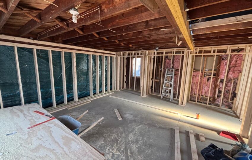 Open framing and insulated walls with plastic sheeting over the floor during a home renovation