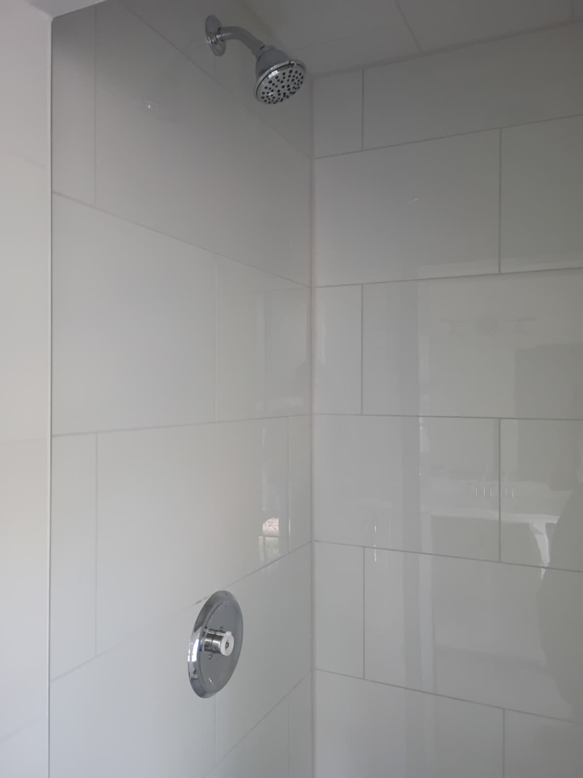 Shower walls in large white rectangular tile with a chrome shower head and valve