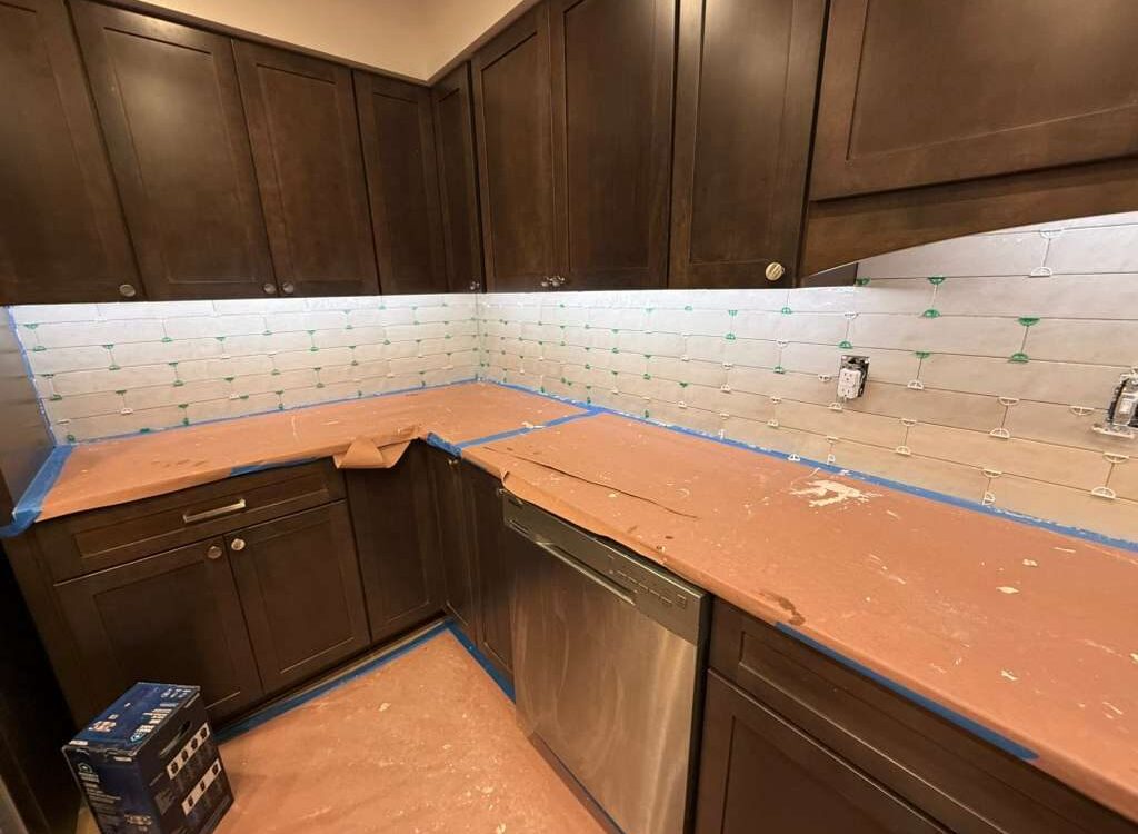 U shaped kitchen with dark espresso shaker cabinets and white subway backsplash, counters covered during install
