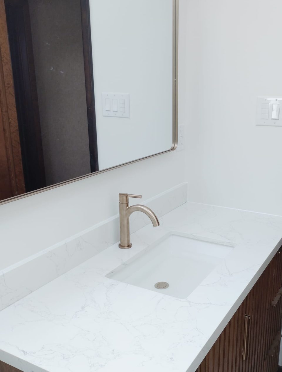 Wood vanity with a white quartz top, undermount sink, brass faucet and a large framed mirror