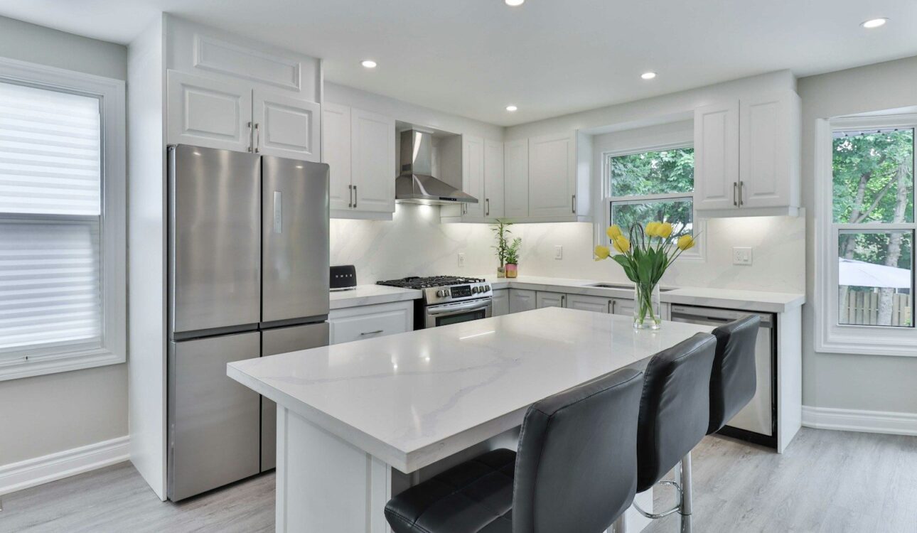 White kitchen with an island, black counter stools, stainless refrigerator and white quartz counters