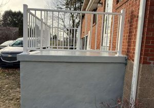 Back porch concrete restoration featuring a smooth gray surface and a custom white railing, showcasing enhanced safety and modern aesthetics.