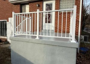 Back porch concrete restoration featuring newly refinished gray concrete surface and custom white railing system for enhanced safety and aesthetics, located in Pittsburgh.