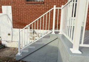 Back porch concrete restoration featuring newly refinished gray concrete steps and custom white railing, enhancing safety and aesthetics.