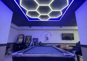 Custom LED hexagonal ceiling design in Shop 724 Barbershop, featuring blue illumination and modern interior aesthetics, with a pool table and arcade machines in the background.