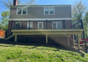 Rear view of a raised deck with gray decking and black railings on a brick home