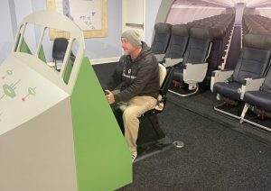 Cockpit style flight simulator beside rows of airline seating