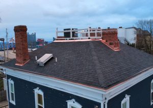 Complete roof replacement in Mt. Washington featuring premium architectural shingles and custom copper flashing, with visible chimney stacks and a rooftop deck railing.