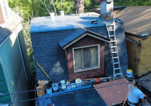 Crew on a ladder finishing new shingles around a dormer window