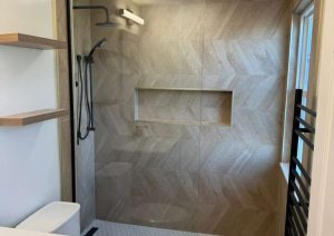 Walk-in shower with a linear drain, shelf and black rain shower head