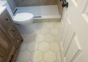 White hexagon floor tile beside a wood vanity and a small shower threshold