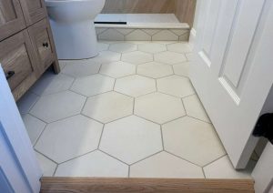 Large white hexagon floor tile with a wood threshold at the bathroom door