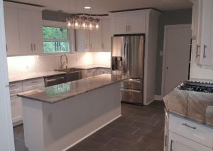Modern kitchen remodel featuring custom white cabinetry, gray quartz countertops, large island for meal prep and gathering, stainless steel appliances, and designer lighting in an open-concept layout.