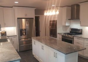 Modern kitchen remodel featuring white shaker cabinets, gray quartz countertops, stainless steel appliances, and a large central island with elegant lighting.