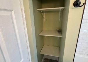 Built-in bathroom storage nook with shelves above gray hex floor tile