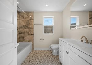 Modern bathroom renovation featuring a white vanity with dual sinks, a spacious bathtub, and stylish herringbone tile flooring, showcasing the transformation of an outdated space in a complete home renovation by JL Home Builders in Etna.