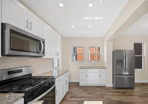 Modern kitchen renovation with white cabinetry, stainless steel appliances, and new flooring in a bright, airy space, showcasing a complete home transformation in Etna by JL Home Builders.