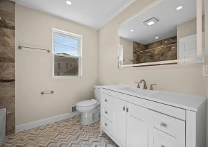 Modern bathroom renovation featuring a white vanity, large mirror, and stylish herringbone tile flooring, showcasing the transformation of an outdated space into a contemporary, move-in ready home in Etna.