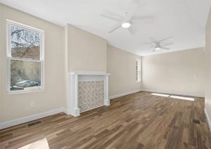 Bright and spacious living room featuring new hardwood flooring, modern ceiling fans, and a decorative fireplace, showcasing the complete home renovation by JL Home Builders in Etna.